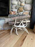 Handcrafted deer antler firewood holder holding firewood beside a stone fireplace